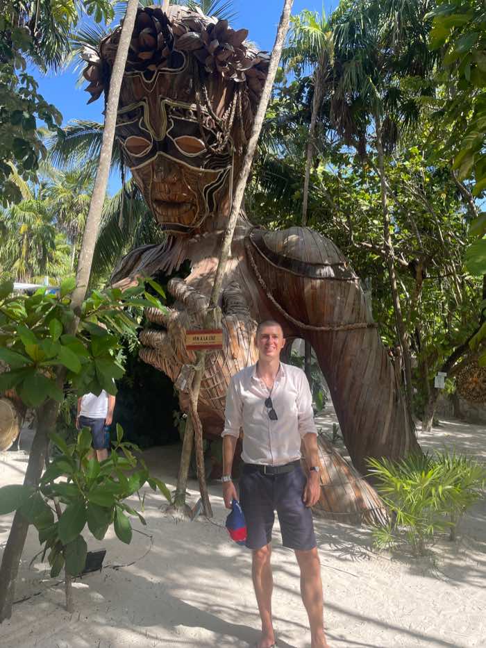 Ladislas Maurice standing in front of wooden statue Ladislas à Tulum au Mexique